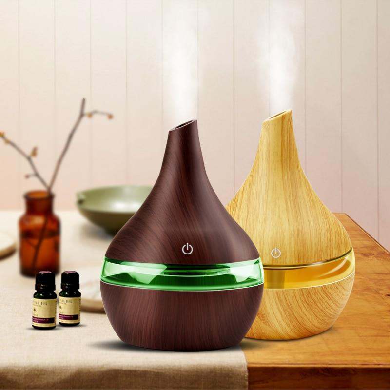 Two wood grain USB aromatherapy humidifiers with adjustable mist and LED lighting on a table next to essential oil bottles